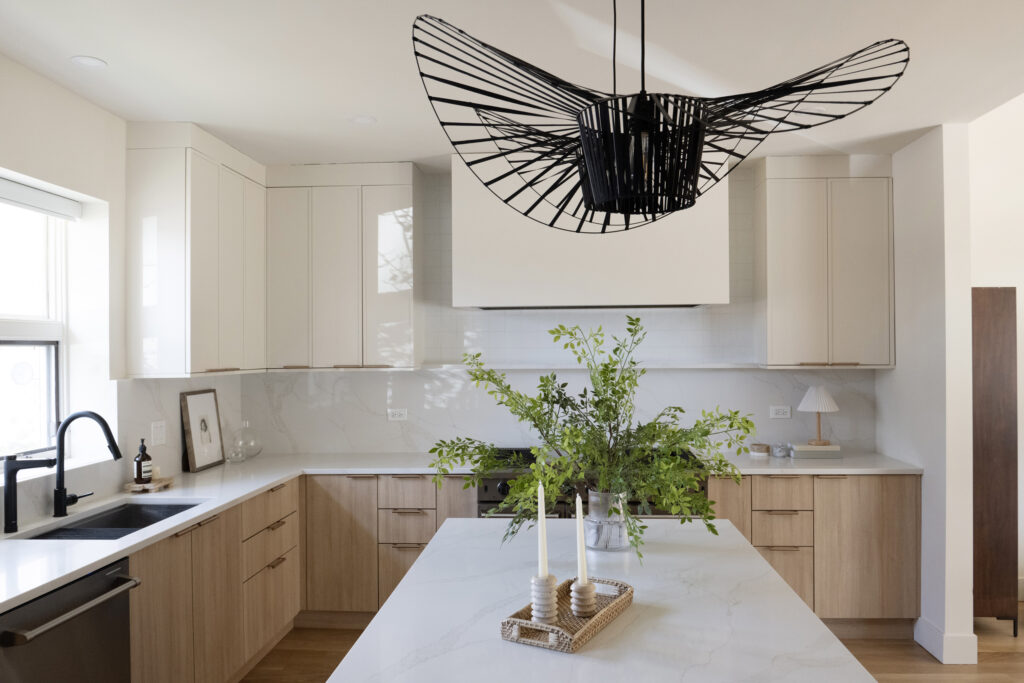 Luxury modern kitchen with custom light wood cabinetry, white stone backsplash, open shelving, and styled greenery on the island.
